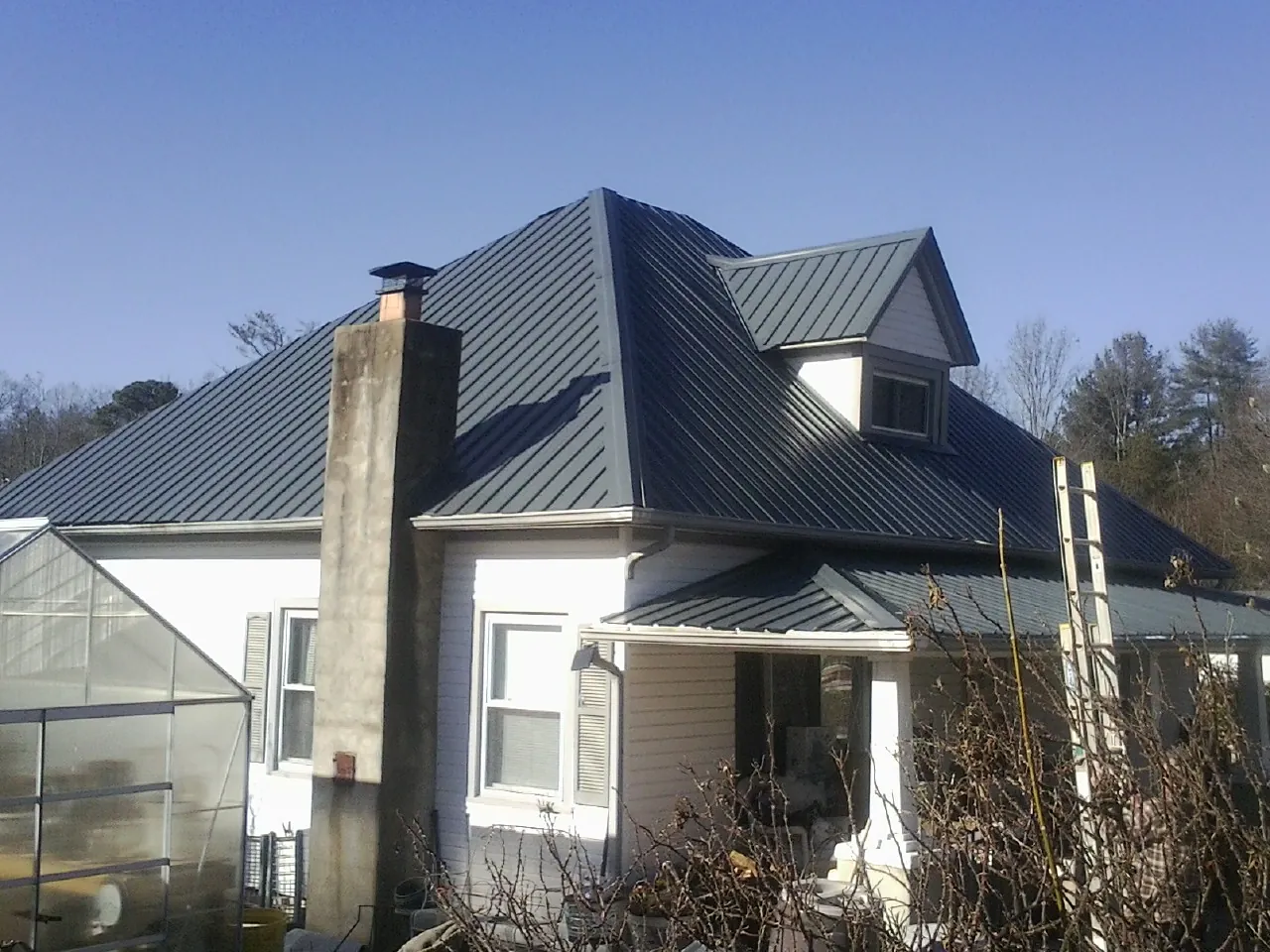 Dark blue standing seam metal roof on a white farmhouse with dormer — Slate & Tile Roof Repair by Roofing Brothers in Baldwin Park