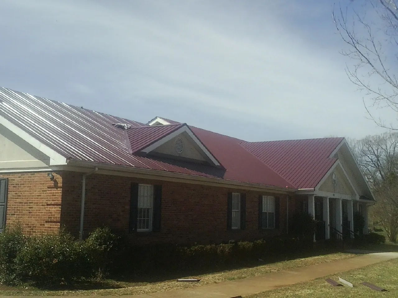 Red metal roof with gabled entries on a long brick building, from a Hail Damage Roof Repair job in Baldwin Park