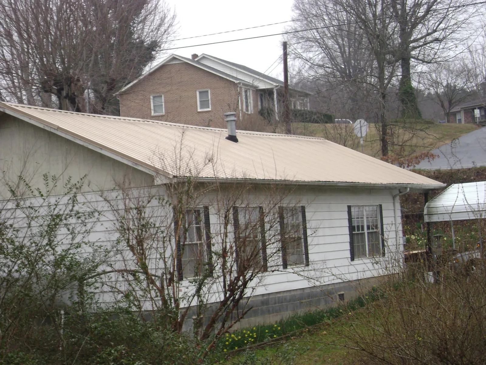 Tan metal roof on a white sided house set into a hillside — Commercial Roofing by Roofing Brothers in Baldwin Park